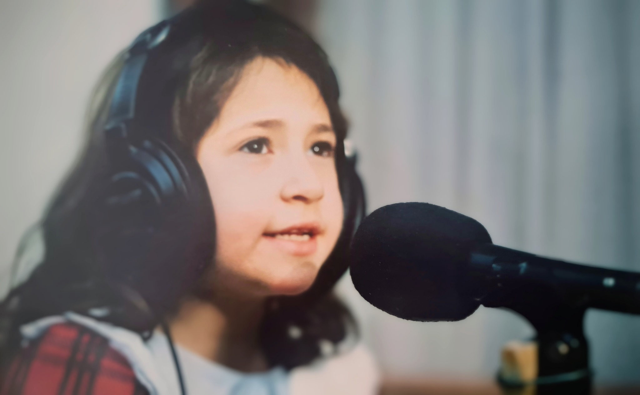 Trini as a child, wearing headphones and speaking into a microphone