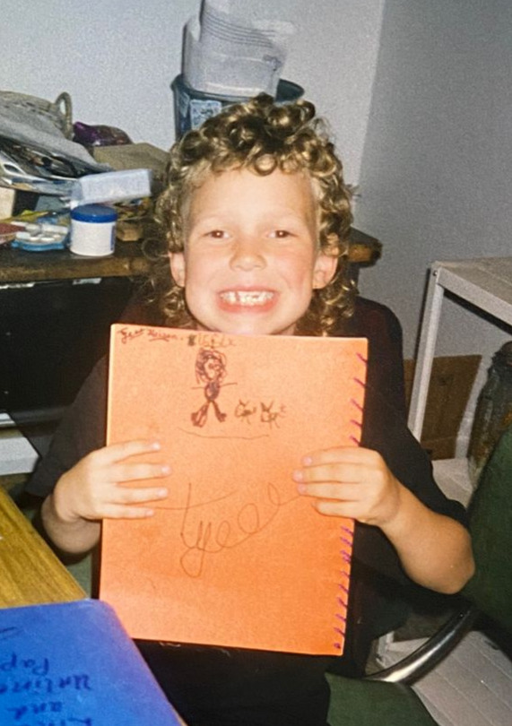 Tyler as a child, smiling and holding a handmade book